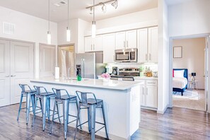 A modern kitchen with white cabinets, stainless steel appliances, and a central island with bar stools.