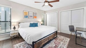 Une chambre à coucher comprenant un lit, un ventilateur de plafond, une table de chevet avec une lampe, une chaise et une table.