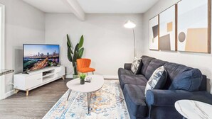 Un salon moderne avec un téléviseur à écran plat, un canapé bleu foncé, une table basse blanche et un tapis à motifs.