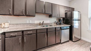 Una cocina moderna con armarios oscuros, un refrigerador de acero inoxidable, encimera de granito y lavavajillas.