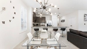 A modern kitchen with a central island, white cabinetry, and a dining area with a glass table and chairs.