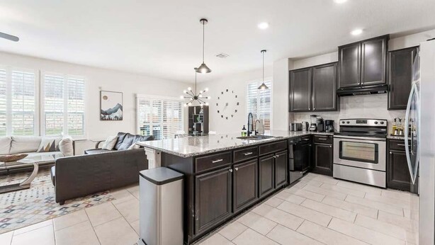 A modern kitchen with dark cabinetry, a central island, stainless steel appliances, and a large window providing natural light.