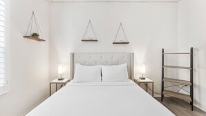 A neatly arranged bedroom with a large bed, bedside tables, hanging shelves, and a ladder against the wall.
