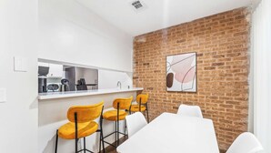 A modern kitchen with white cabinets, a white countertop, and a brick wall. There are four yellow chairs and a white table. - Prime SoCo cozy 1BR king suite w/ pool, parking (Austin)