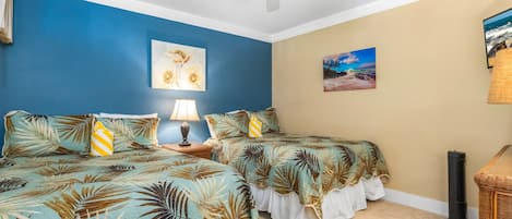A bedroom with two beds, a ceiling fan, and artwork on the walls.