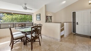 A dining area with a glass-top table and wicker chairs, a ceiling fan, and a view of greenery outside. - Wailea Ekolu, #914 2 Bedroom Condo by RedAwning (Kihei)