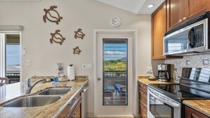 A kitchen with granite countertops, stainless steel appliances, and a view through a door to a balcony. - Wailea Ekolu, #914 2 Bedroom Condo by RedAwning (Kihei)