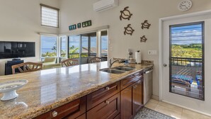 A kitchen with a large island, a dining area with chairs, a view of the ocean, and a door leading to a balcony. - Wailea Ekolu, #914 2 Bedroom Condo by RedAwning (Kihei)