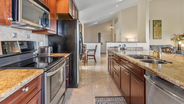 A modern kitchen with granite countertops, stainless steel appliances, and wooden cabinetry. - Wailea Ekolu, #914 2 Bedroom Condo by RedAwning (Kihei)