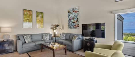 A living room with a grey sofa set, a coffee table, a TV, and artwork on the walls.