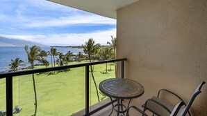 Un balcone con tavolo e sedie, vista su un campo da golf e l'oceano.