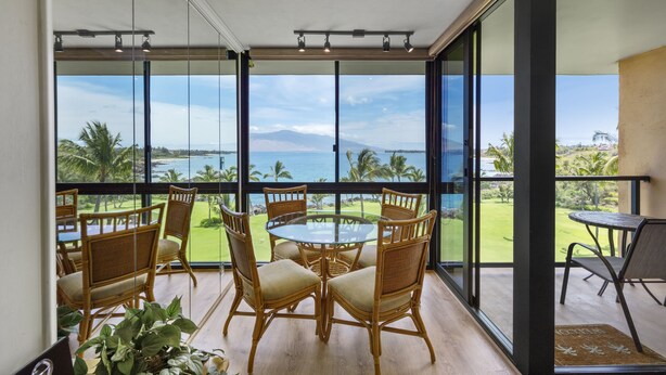 Ein Balkon mit Glastisch und Stühlen, der auf eine Küstenlandschaft mit Palmen und Meerblick blickt.