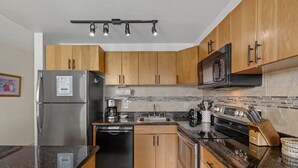 Una cucina moderna con mobili in legno, elettrodomestici in acciaio inossidabile, un piano di lavoro nero e un forno a microonde integrato.