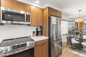 A modern kitchen with stainless steel appliances, wooden cabinets, and a glass dining table.