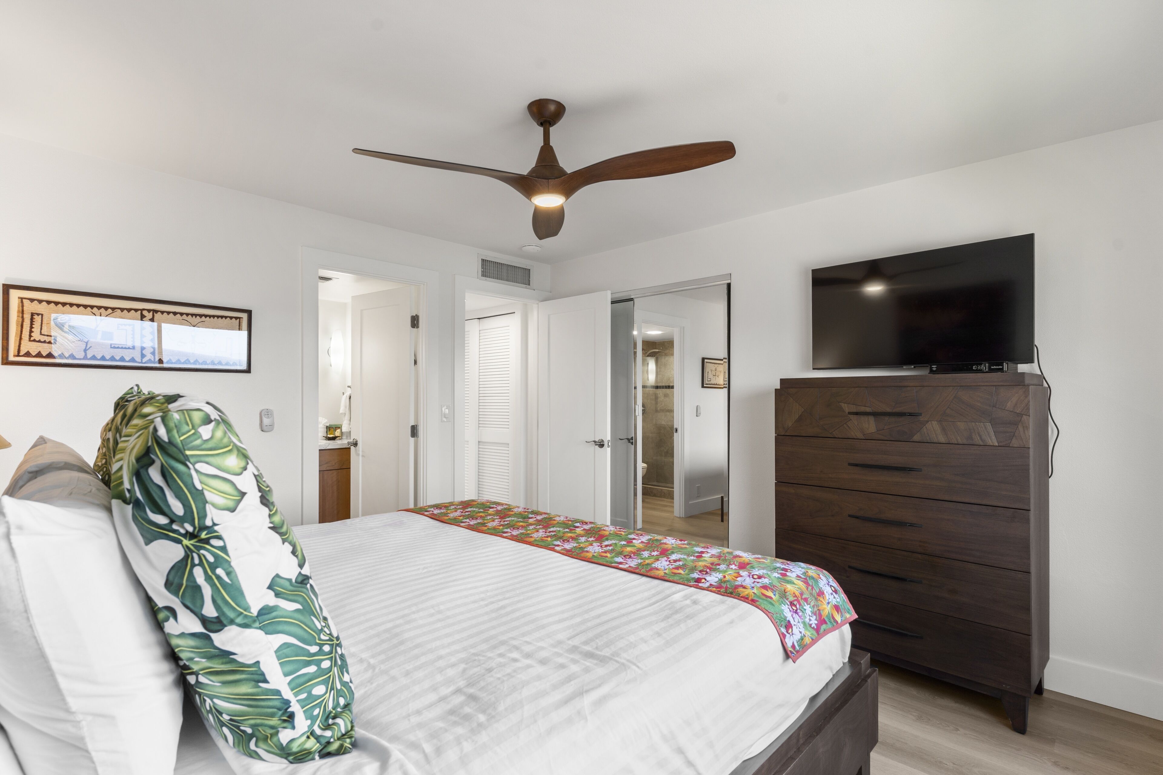 A bedroom with a bed, a dresser, a ceiling fan, and a TV.