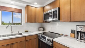 A modern kitchen with wooden cabinets, stainless steel appliances, a built-in oven, and a window with a view of greenery.