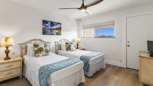 A hotel room with two beds, a ceiling fan, a painting, a window with a view, and a television on a side table.