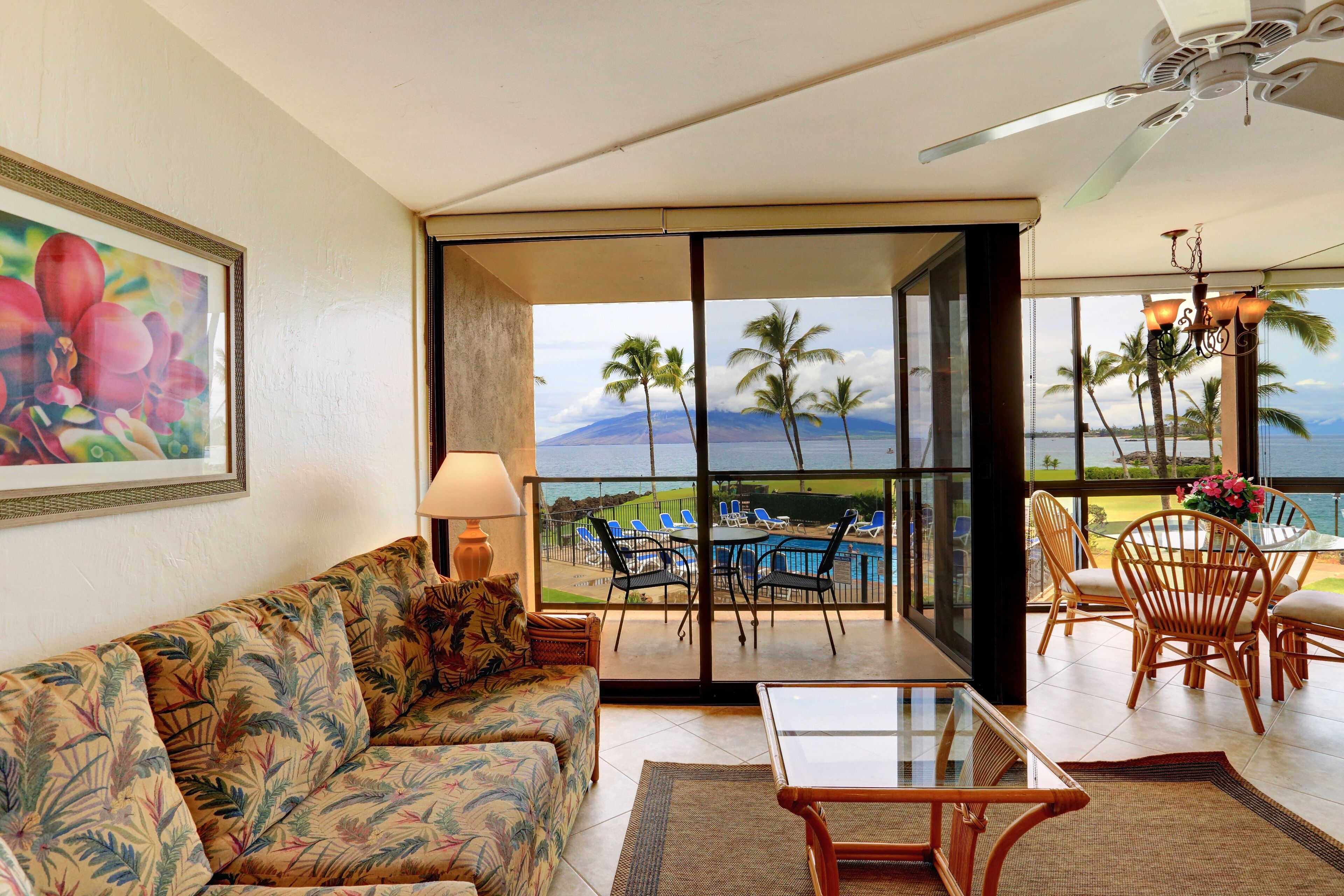 A room with a sofa, a table, and a view of a pool and palm trees.