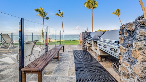 A patio with a stone grill, a wooden bench, and a view of the ocean. - Kihei Surfside, #205 1 Bedroom Condo by RedAwning (Kihei)