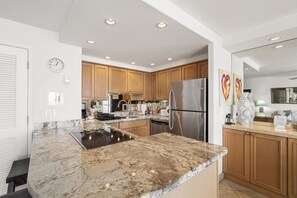 A modern kitchen with granite countertops, stainless steel appliances, wooden cabinets, and a built-in oven. - Kihei Beach, #603^ 1 Bedroom Condo by RedAwning (Kihei)