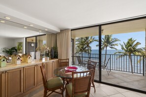 A dining area with a glass table and chairs, a kitchen counter with decorative items, and a view of the sea through large windows.