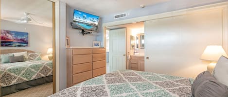 Une chambre à coucher comprenant un lit, une commode, un téléviseur et un ventilateur de plafond.