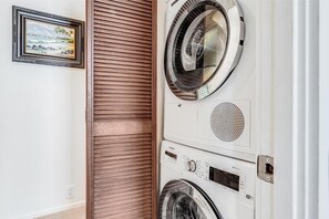 A laundry room with a wall-mounted washer and dryer, a wooden door, and a framed picture on the wall. - Wailea Elua, #1402^ 1 Bedroom Condo by RedAwning (Kihei)