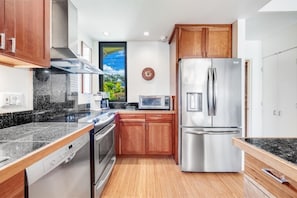 A modern kitchen with wooden cabinets, stainless steel appliances, and a black granite countertop.
