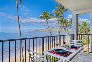 Un balcone con un tavolo apparecchiato per due, affacciato su una spiaggia con palme e vista sull'oceano.