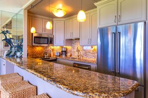 A kitchen with granite countertops, stainless steel appliances, and pendant lighting. - Kihei Surfside, #411 1 Bedroom Condo by RedAwning (Kihei)