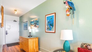 A room with a wooden dresser, a glass table with a teal lamp, and two framed pictures on the wall.