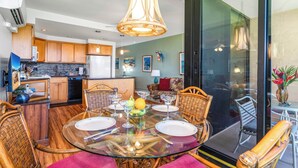 A modern kitchen with wooden cabinets, a dining area with a glass table, and a view through a large sliding glass door.