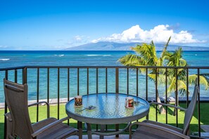 Een balkon met een glazen tafel, twee stoelen en uitzicht op zee en een berg.
