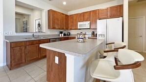A kitchen with wooden cabinets, a white refrigerator, a microwave, and a large island with bar stools. - Villa Marcello 4 Bedroom Home by RedAwning (Kissimmee)