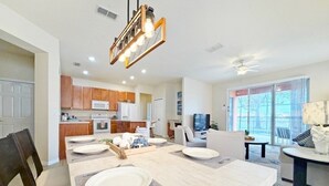 A modern kitchen with wooden cabinets, a dining area with a large table, and a living space with a sofa and TV. - Villa Marcello 4 Bedroom Home by RedAwning (Kissimmee)