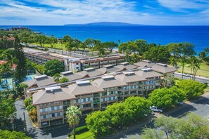 A hotel with multiple buildings, a parking area, and a view of the ocean.