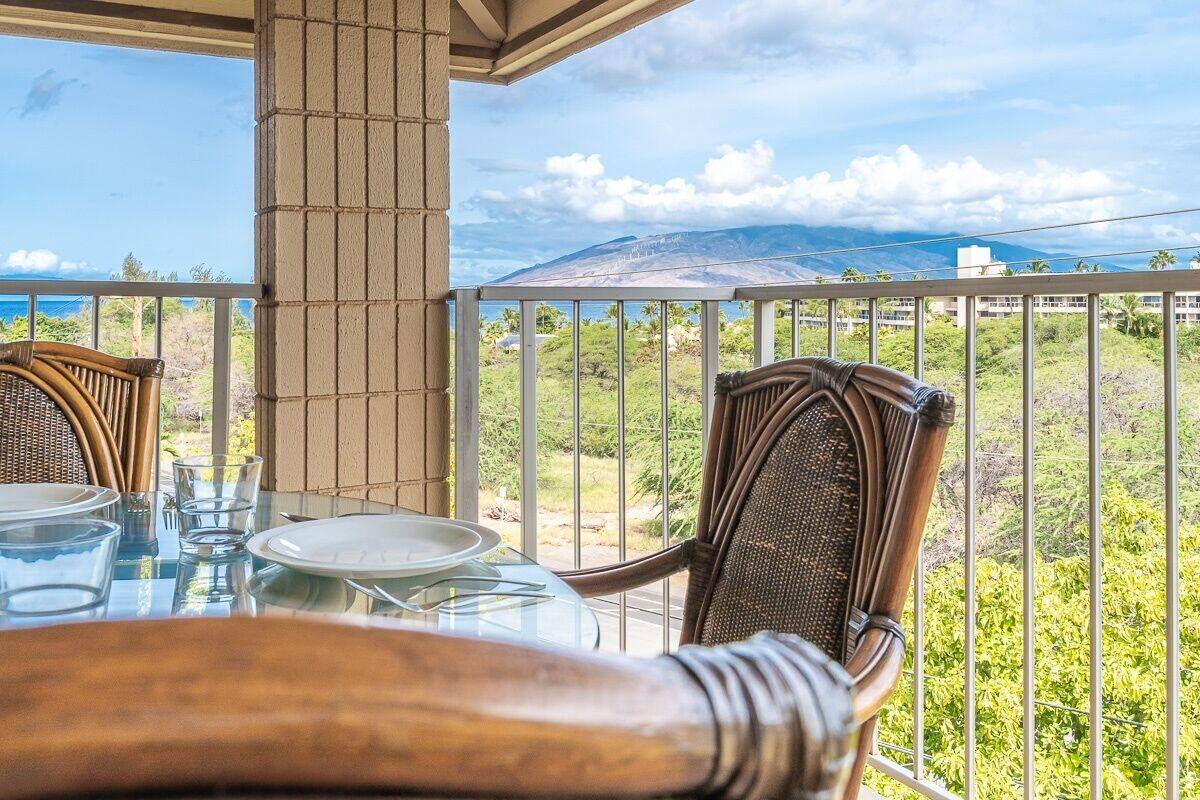 Ein Balkon mit Glastisch und Stühlen mit Blick auf eine gebirgige Landschaft.