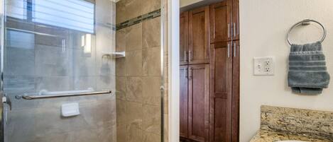 A bathroom with a glass shower enclosure, a granite countertop, a sink, wooden cabinets, and a towel ring.