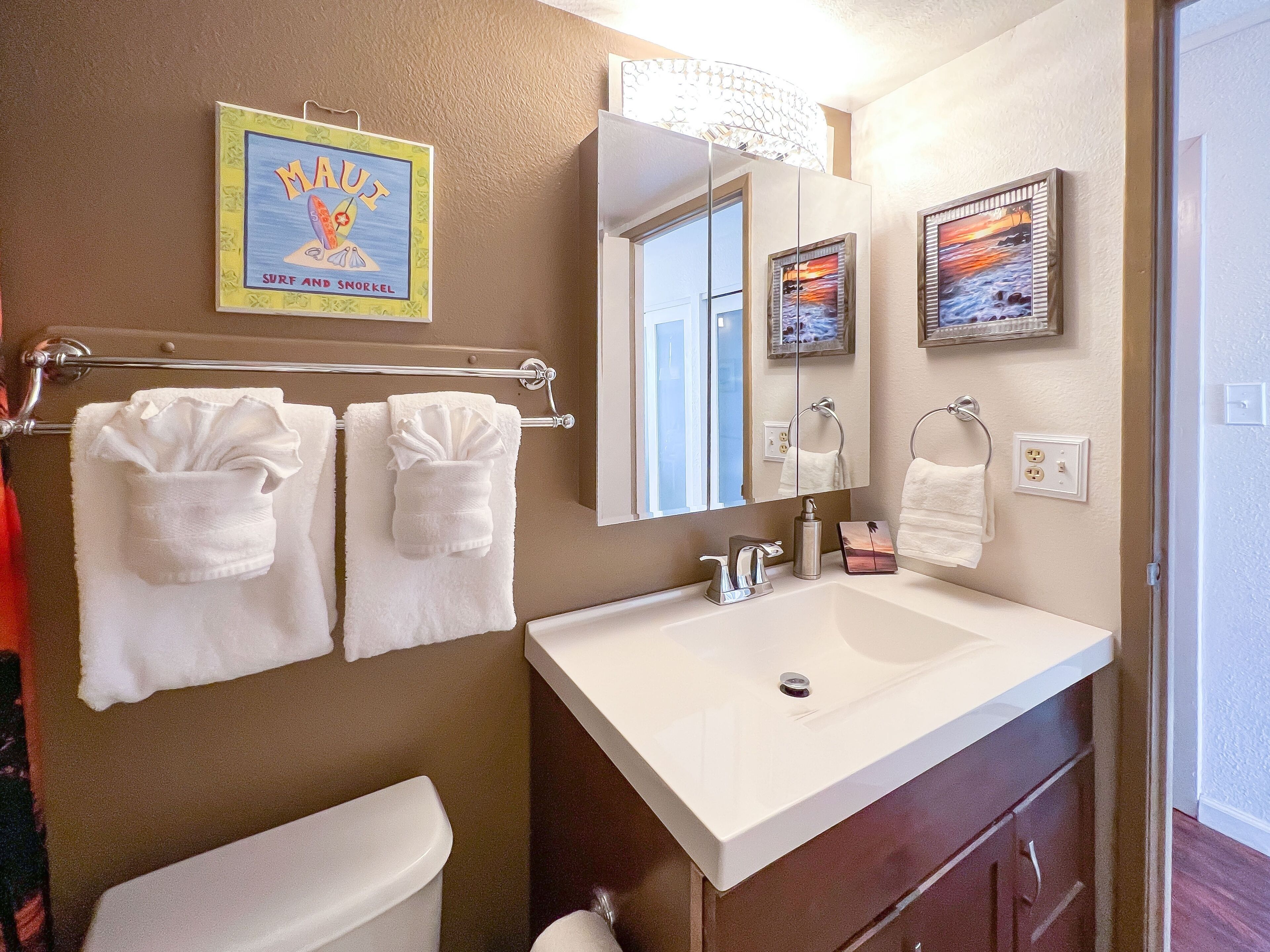 Une salle de bain avec un lavabo blanc, deux serviettes blanches, un tableau représentant une plage et un miroir.