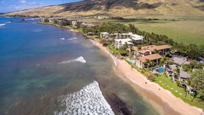 Vista aérea de um resort costeiro com propriedades à beira-mar, uma visão clara do oceano e uma paisagem montanhosa ao fundo.