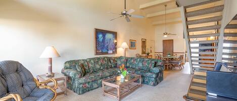 A living room with a sectional sofa, a wicker chair, a glass coffee table, and a dining area with a table and chairs.