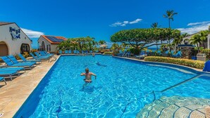 A swimming pool with lounge chairs, palm trees, and a building with a sign. - Maui Hill by Coldwell Banker Island Vacations (Kihei)