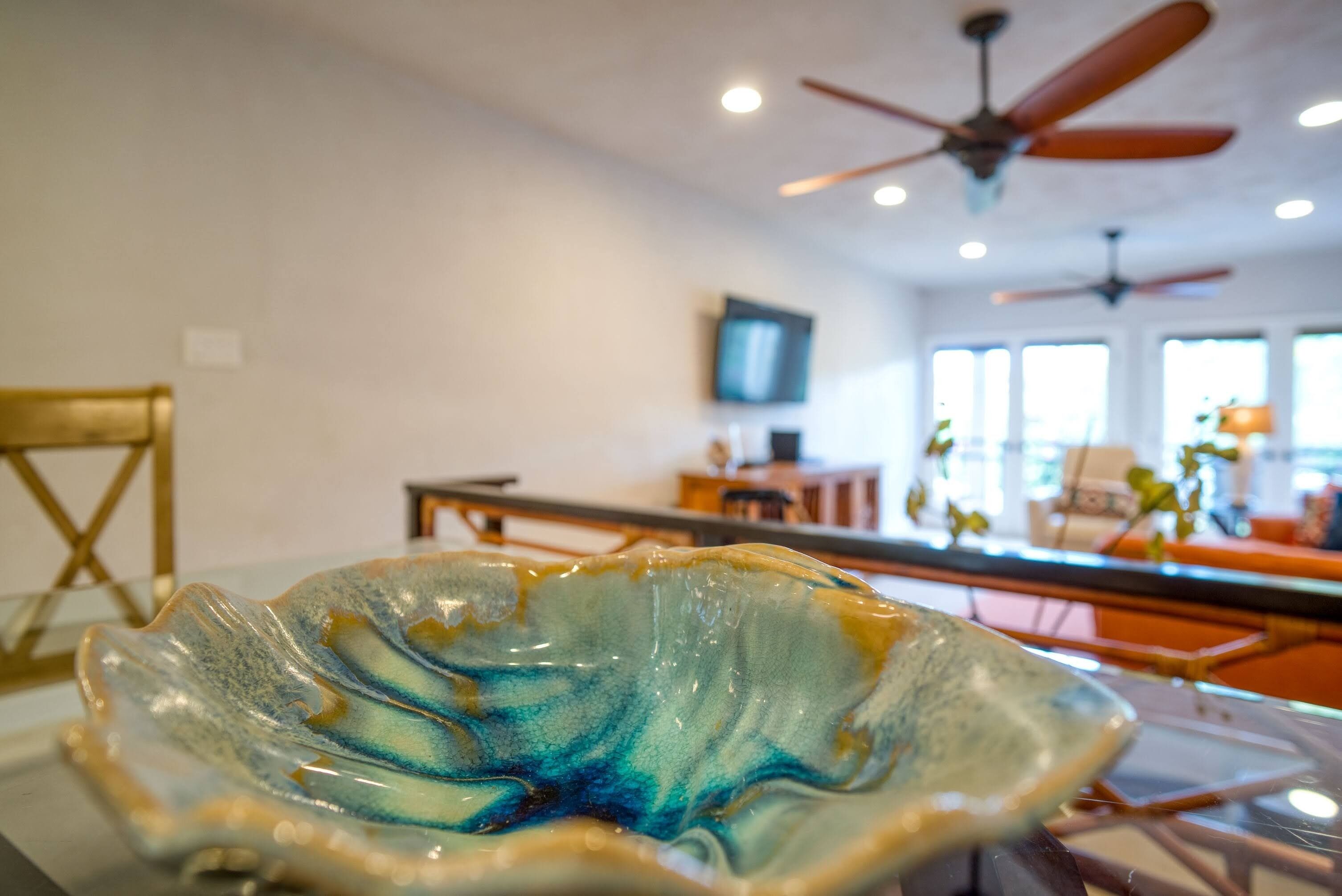 Un salon moderne avec un vase décoratif en verre posé sur une table, un ventilateur de plafond et un téléviseur fixé au mur.