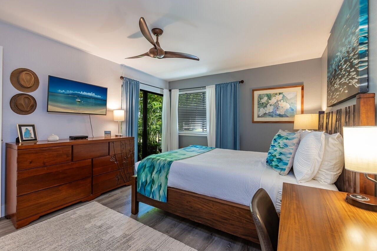 A bedroom with a bed, wooden dresser, ceiling fan, and artwork on the walls.