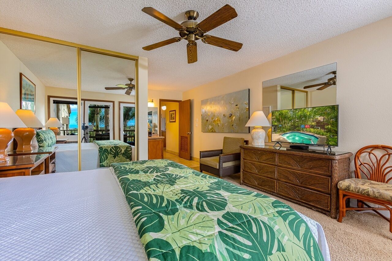 A hotel room with a bed, a television, a dresser, a chair, and a ceiling fan.