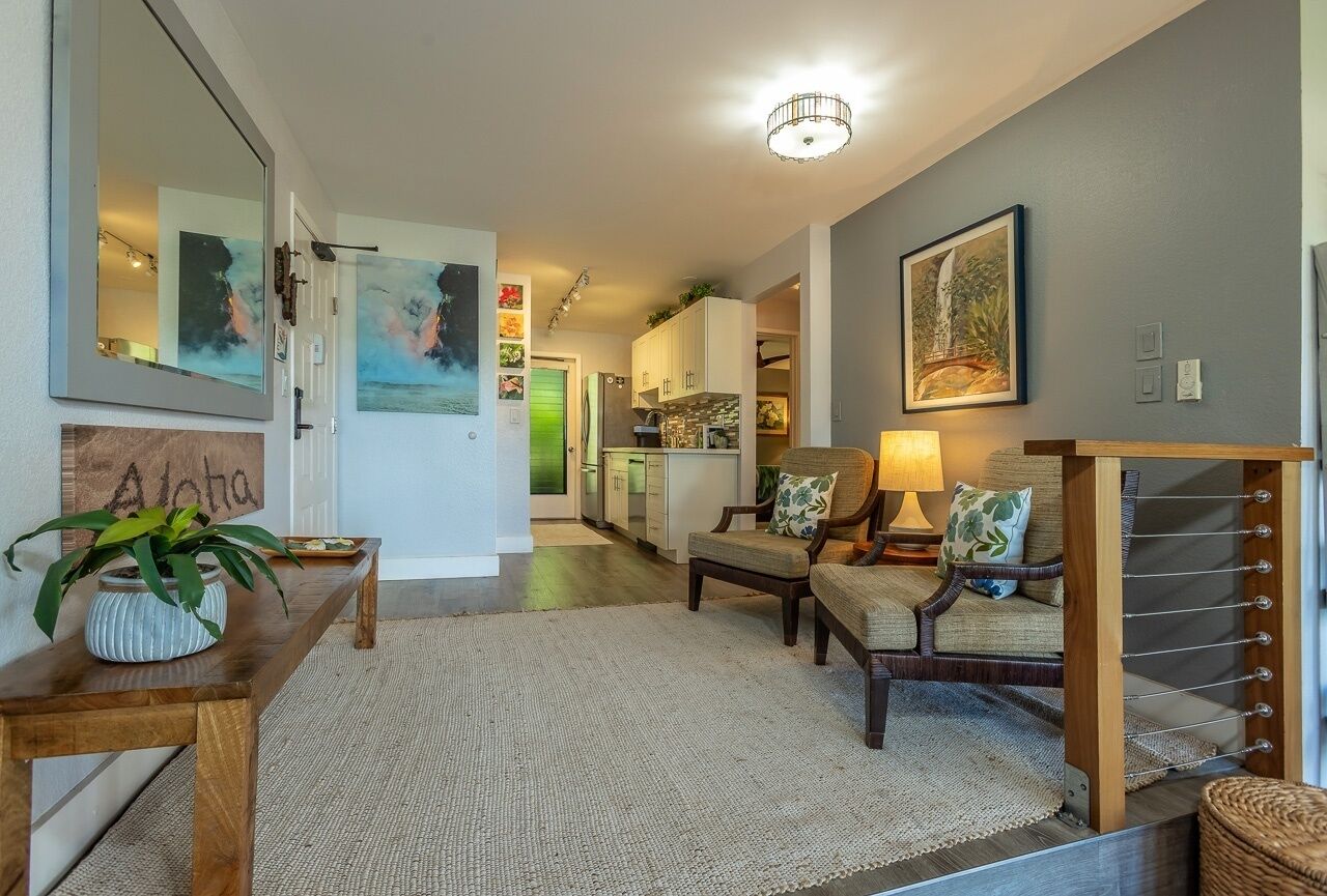 Una sala de estar moderna con un sofá, una mesa de centro y una lámpara. Hay un cuadro en la pared y una planta sobre una mesita auxiliar.