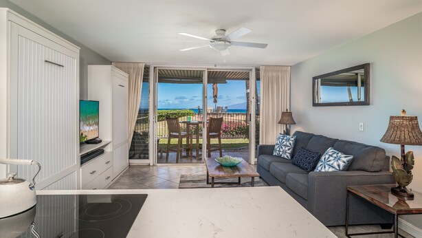 A modern living room with a sofa, coffee table, and TV. There is a balcony with a view of the outdoors.
