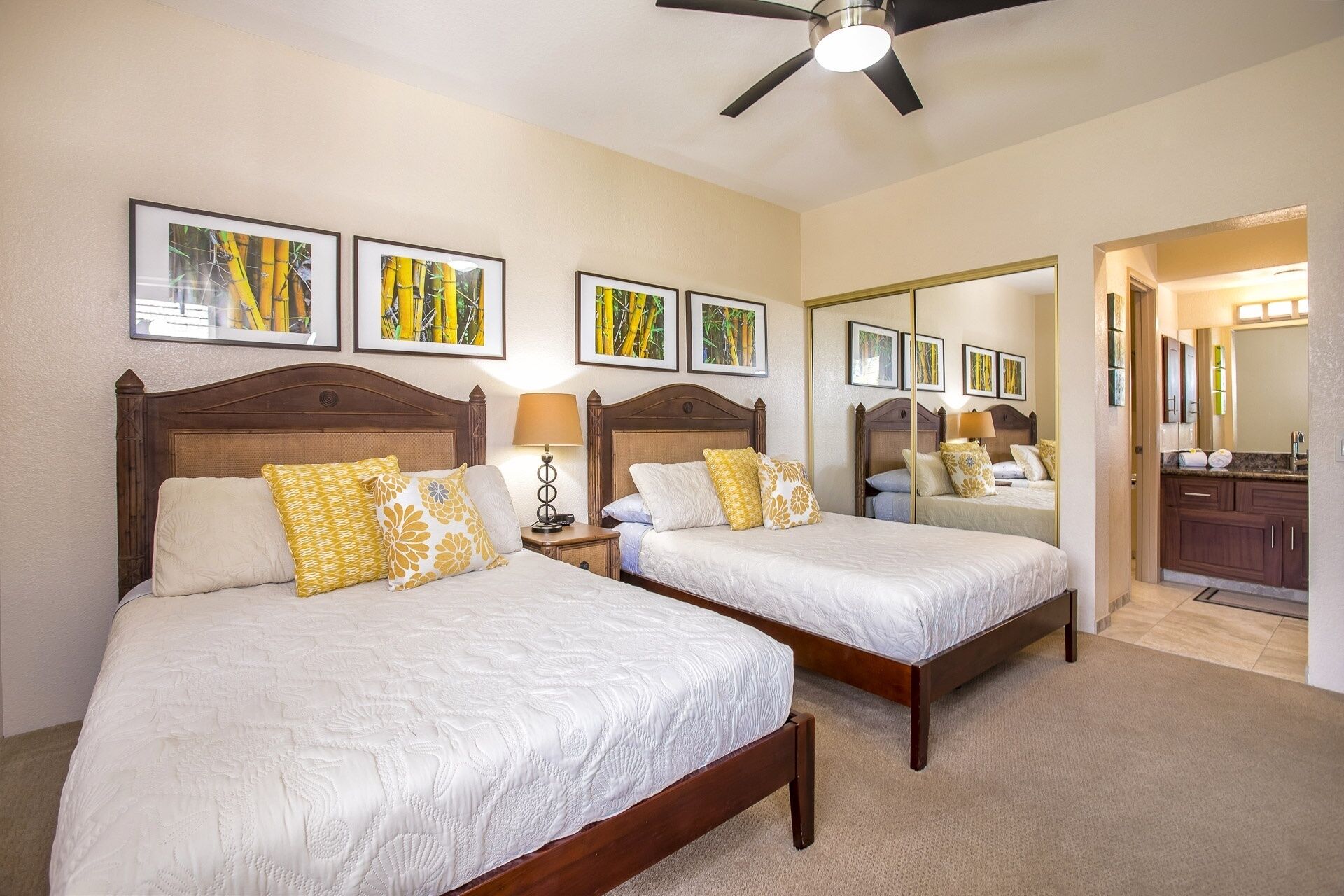 A hotel room with two beds, a ceiling fan, and framed artwork on the wall.