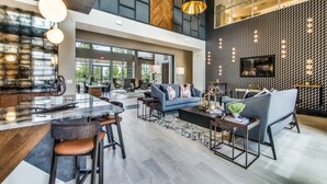 Un hall d’entrée spacieux avec un plafond haut, un espace de détente central avec des canapés et des fauteuils, un coin bar avec des tabourets et un grand téléviseur fixé au mur.