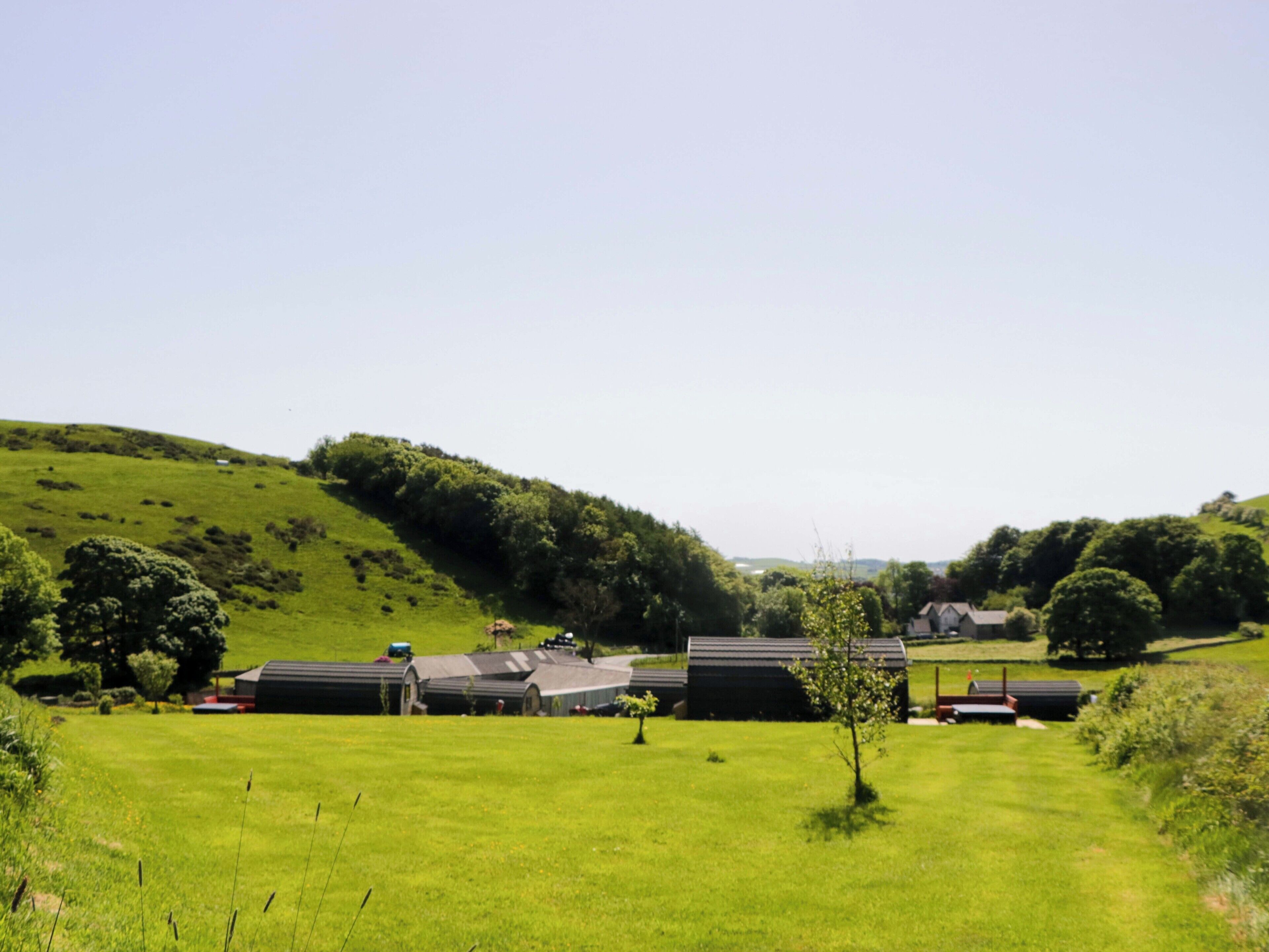 A rural setting with a grassy field, a few trees, and several buildings with flat roofs.